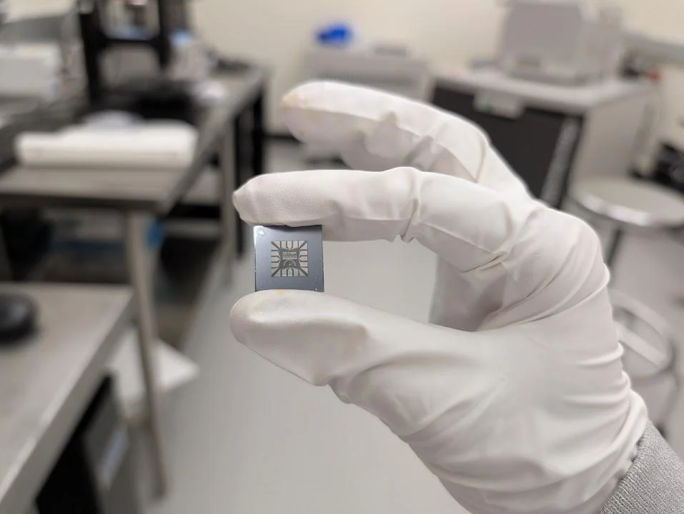 A gloved hand holding a small patterned silicon chip